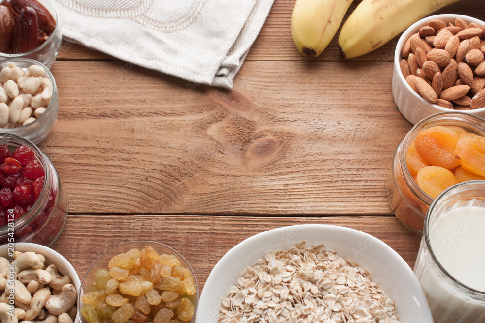 Frame of ingredients for healthy breakfast. Fresh and dried fruits, nuts, milk. Copy space on wooden table.