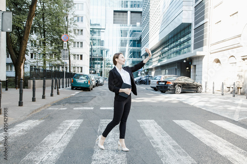 A young woman in a business suit crosses the street. Business woman talking through a mobile phone. A girl with a notepad and a phone near the office. © ibilyk13
