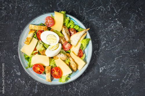 Fresh caesar salad in plate on black stone table. Top