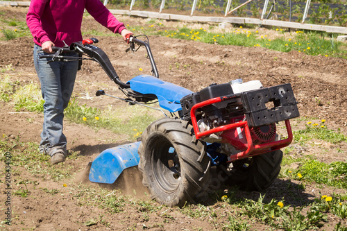 Woman worker driving rototiller tractor unit preparing soil seedbed on outdoor garden