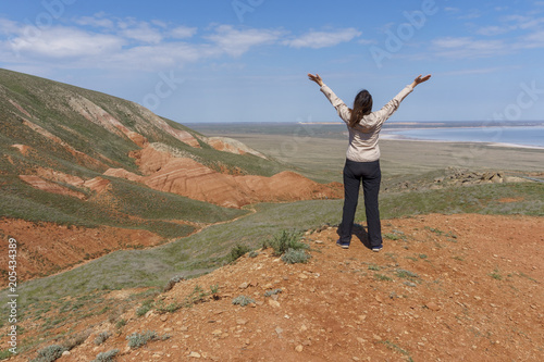 Young active woman standing on top of a mountain, raising her hands to the sky