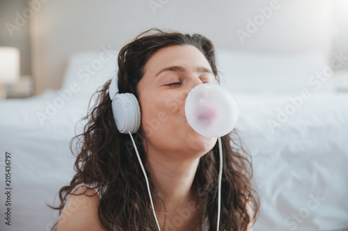 young woman making a bubble from a chewing gum and listening music with headphone