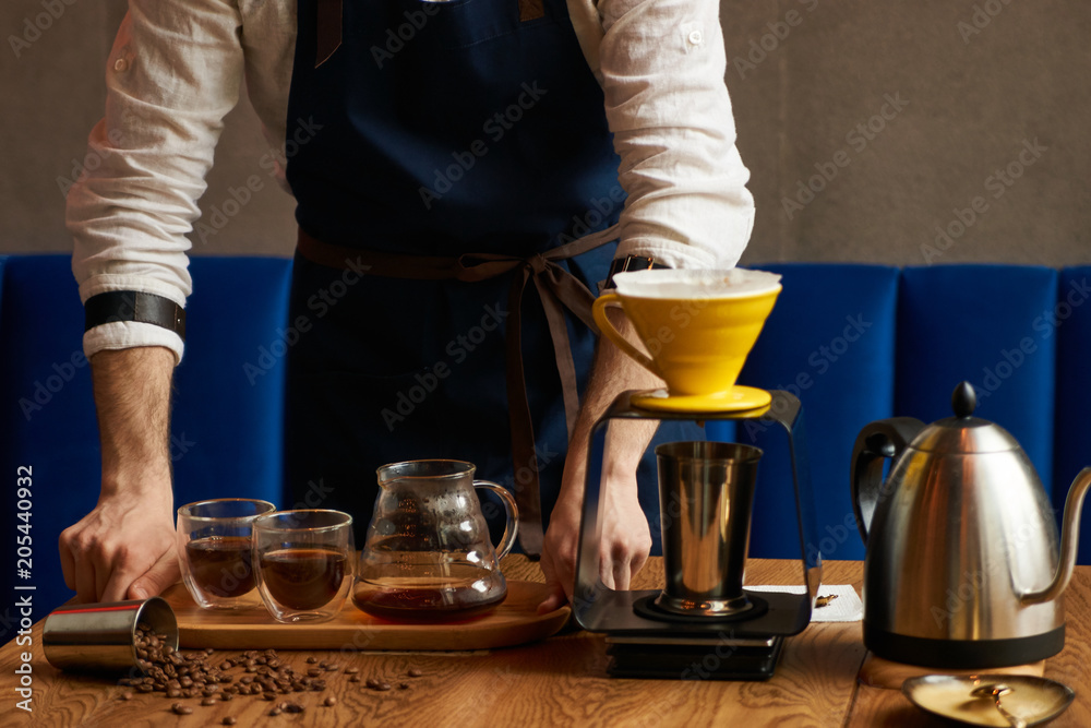 Professional Barista or coffee barman prepares coffee by an alternative method of brewing, pour over, by hot water spilling through a special filter with ground powder