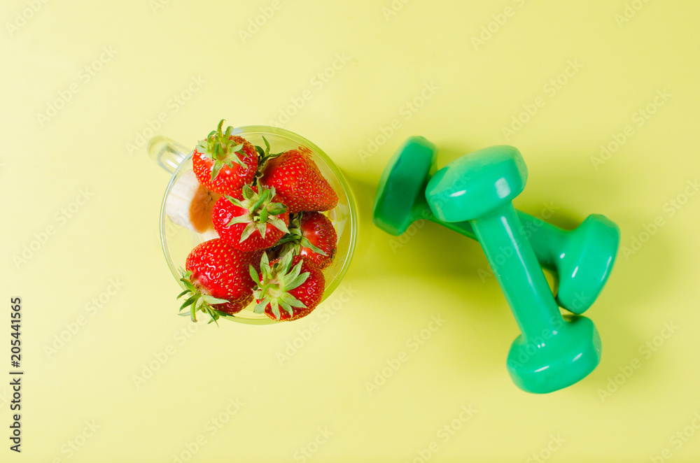 Strawberry and sports dumbbells lie on a light yellow background. The concept of the correct image of zhizi. Diet. Strawberry and sports dumbbells lie on a light yellow background. The concept of the correct image of zhizi. Diet.