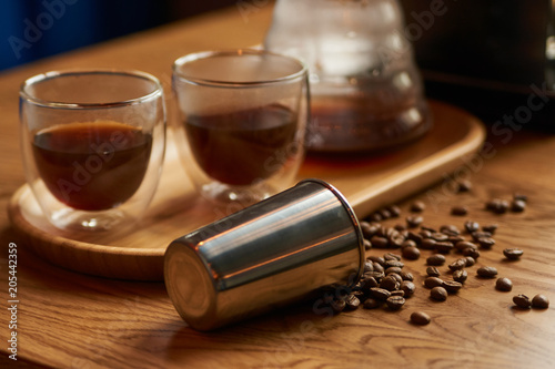 Coffee beans, metal cup and glass cup of coffee drink on wooden table background, close-up.