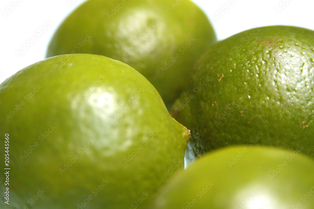 Four whole limes on a white background. Whole limes, shallow depth of field, focus on one lime. Group of limes on a white table in the studio, close up shot. Four whole limes on a white background. Whole limes, shallow depth of field, focus on one lime. Group of limes on a white table in the studio, close up shot.