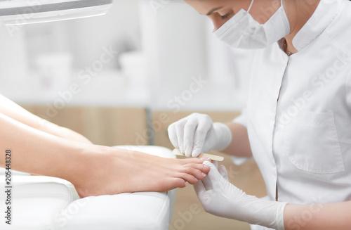 Nail artist in beauty salon polish nails on foot by tool.