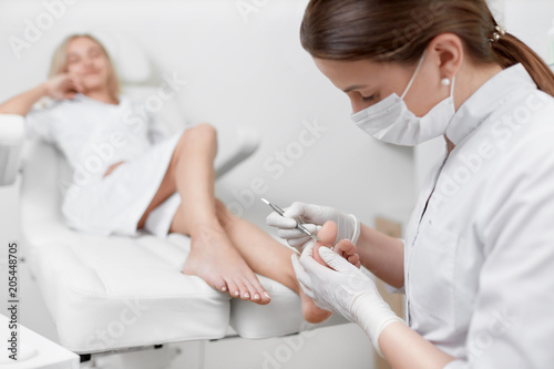 Podiatrist doctor caring about client foot with special iron tool.