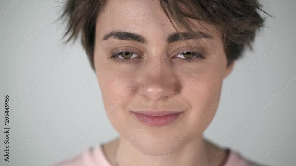 Portrait of a young woman with short brown hair, big eyes and full lips blinking and half smiling to someone off camera. Locked down real time medium shot Portrait of a young woman with short brown hair, big eyes and full lips blinking and half smiling to someone off camera. Locked down real time medium shot