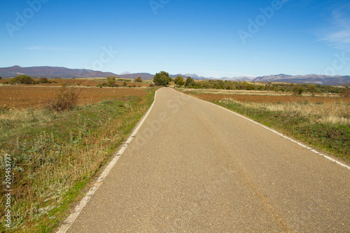 Secondary road in landscape of agricultural land in autumn with hills and mountains in the background 