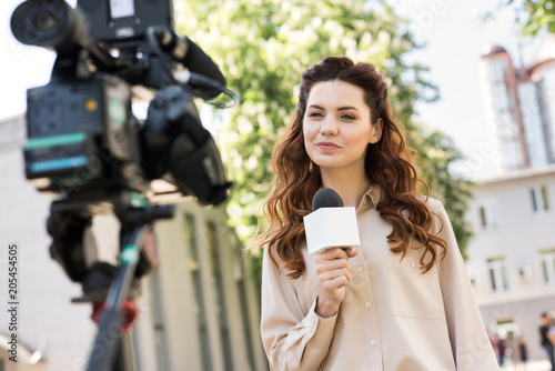 beautiful female journalist with microphone talking to digital video camera photo