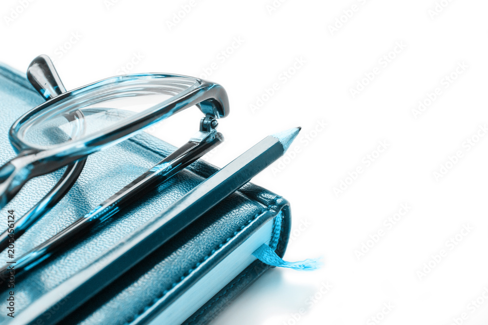 Reading glasses and pencil lie on a notebook on a white background. Reading glasses and pencil lie on a notebook on a white background.