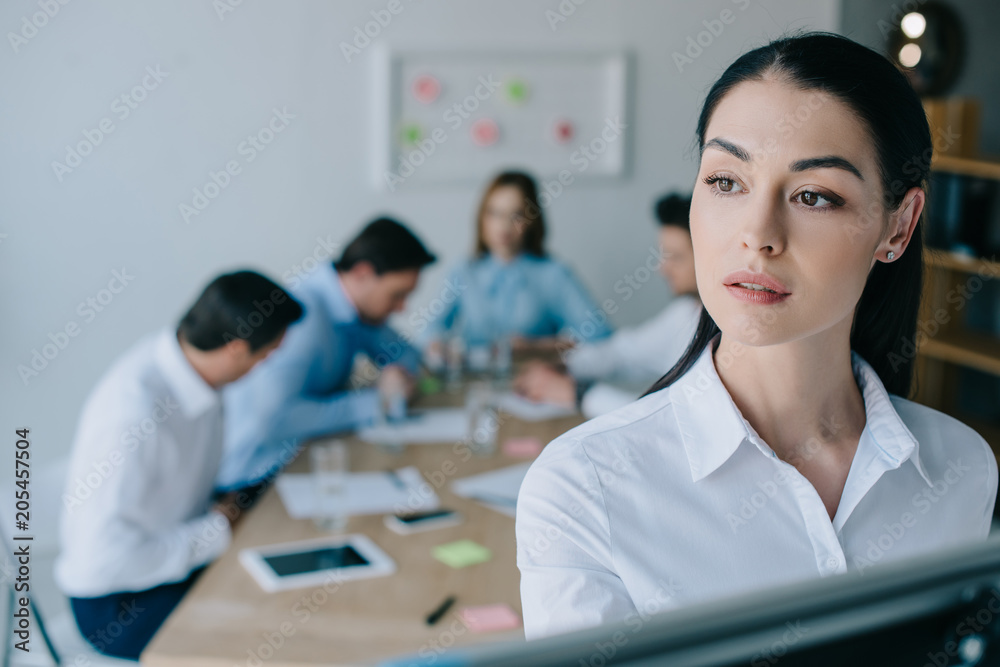 selective focus of pensive businesswoman and colleagues behind at workplace in office