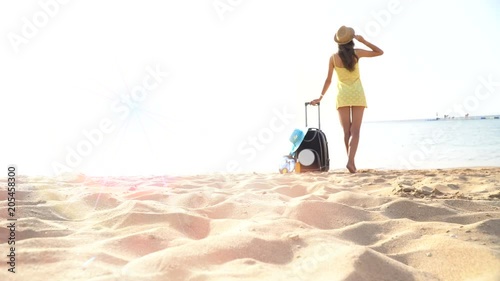beautiful woman in a hat stands on the beach with a suitcase and looks into the distance. 4k video photo