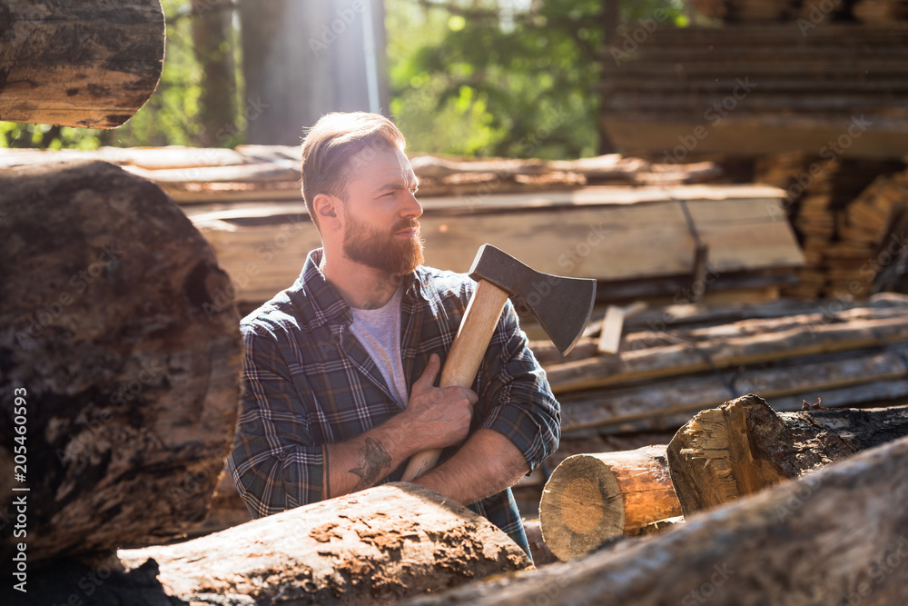 side view of lumberjack in checkered shirt with tattooed hand holding axe at sawmill side view of lumberjack in checkered shirt with tattooed hand holding axe at sawmill
