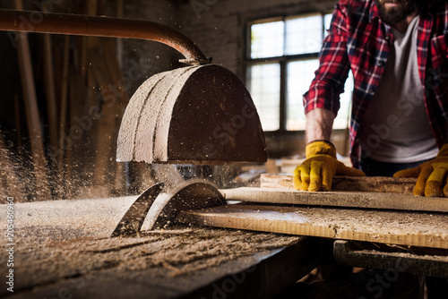 cropped image of carpenter in protective gloves  using machine saw at sawmill photo