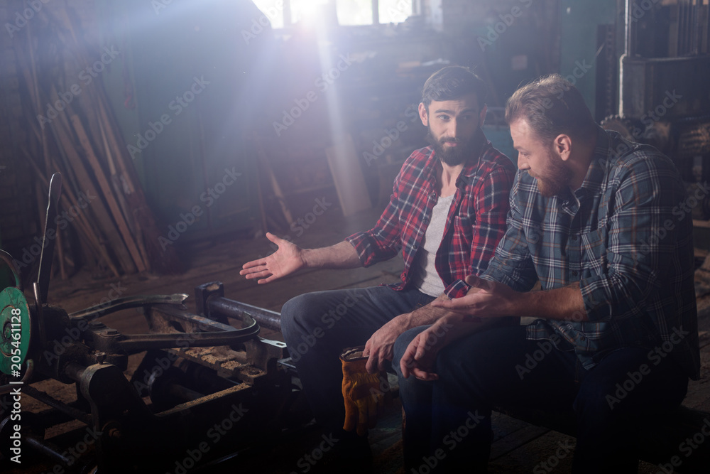 bearded worker pointing on machine to colleague at sawmill