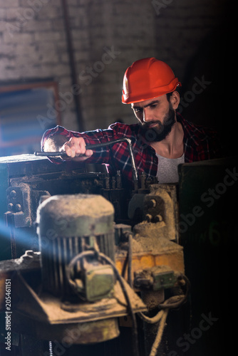 worker in protective helmet repairing machine tool at sawmill