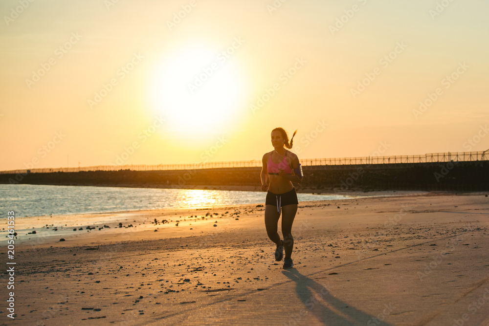 silhouette of sportswoman with smartphone in running armband case jogging on beach against sunlight silhouette of sportswoman with smartphone in running armband case jogging on beach against sunlight
