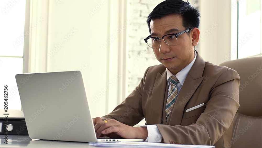 An Asian businessman Working on a laptop looking intense and seriousness about the company’s sales figures performance An Asian businessman Working on a laptop looking intense and seriousness about the company’s sales figures performance