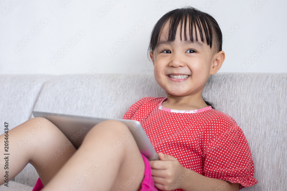 Asian Chinese little girl sitting on the sofa playing digital tablet Asian Chinese little girl sitting on the sofa playing digital tablet