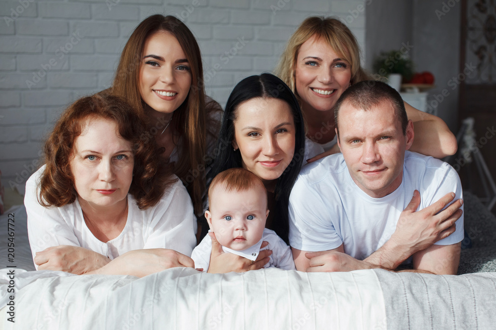 Big family of six people with a young man and grandmother lying in bed and looking at the camera