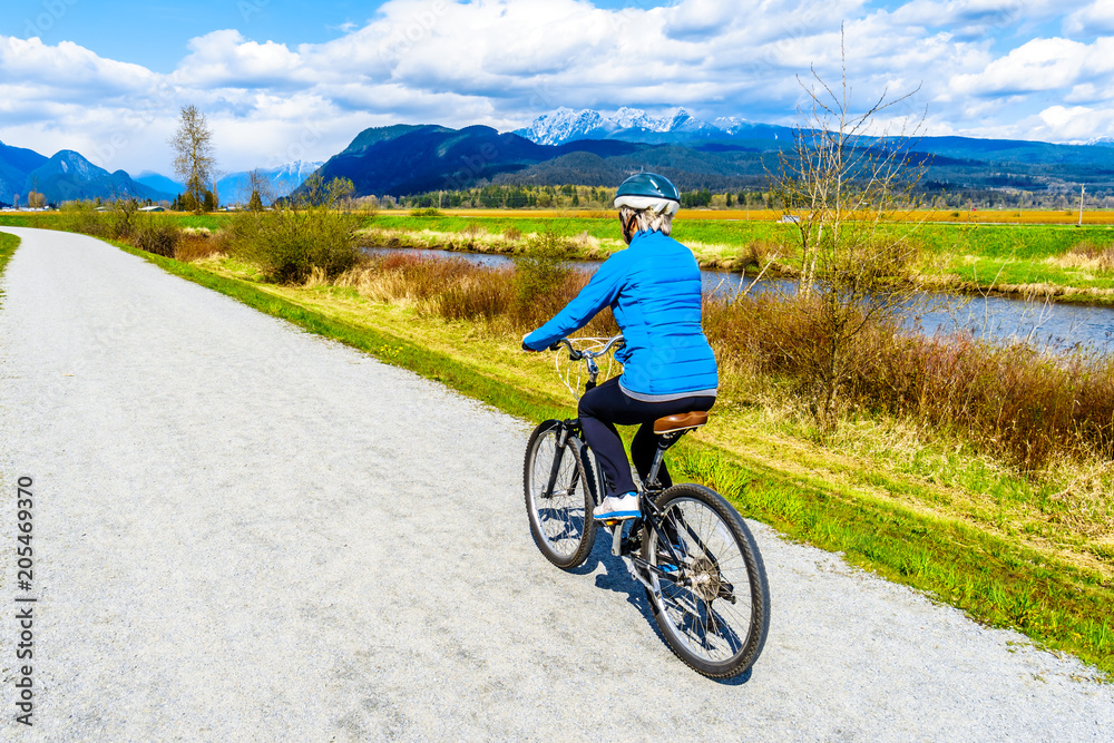 Senior woman biking along the Alouette River on the dyke surrounding Pitt Polder at the town of Maple Ridge in British Columbia, Canada Senior woman biking along the Alouette River on the dyke surrounding Pitt Polder at the town of Maple Ridge in British Columbia, Canada