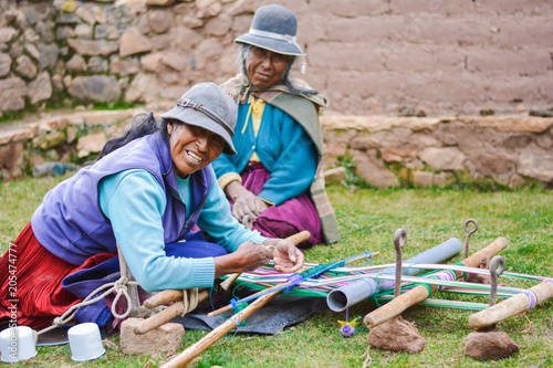 Happy native american mother and daughter weaving authentic aymara cloth.
