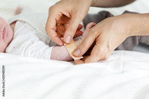 mother or doctor or nurse is putting a plaster on the baby hand