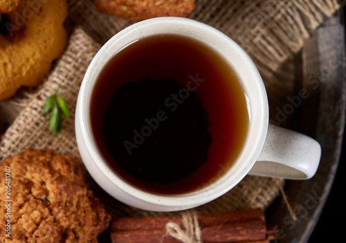 Top view festive composition with a cup of hot tea, cookies and spicies on a wooden barrel, selective focus, close-up