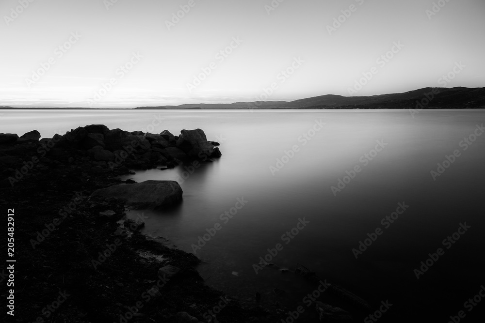 Dusk on a lake, with rocks in the foreground, perfectly still wa