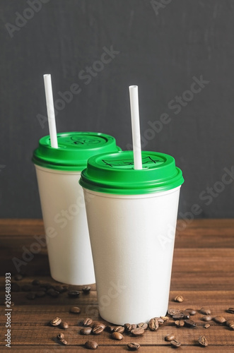 two white plastic coffee cups with a green lid on a wooden table with scattered coffee beans
