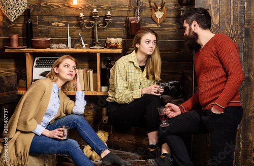 Friends, family spend pleasant evening, interior background. Sincere conversation concept. Girls and man on happy faces hold metallic mugs, talking. Family enjoy conversation in gamekeepers house
