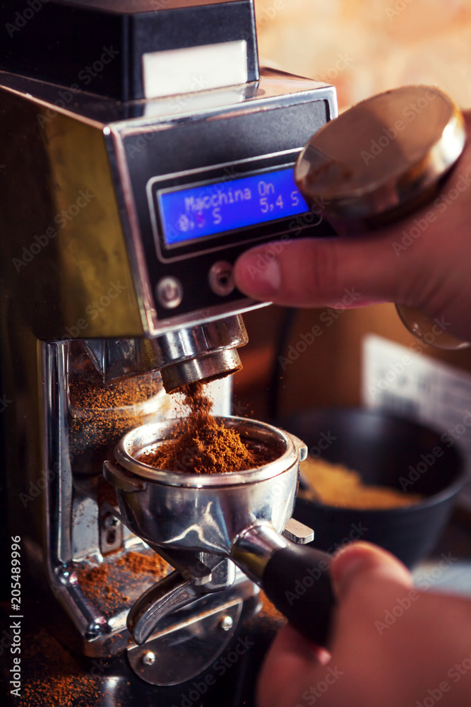 Cropped image of barista using coffee grinder holding portafilter with ground coffee.