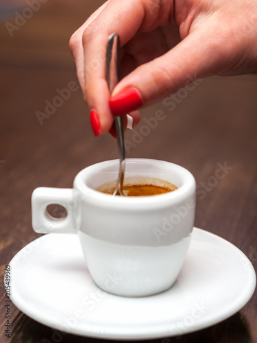 Close up of female hand with cup of espresso coffee and spoon.