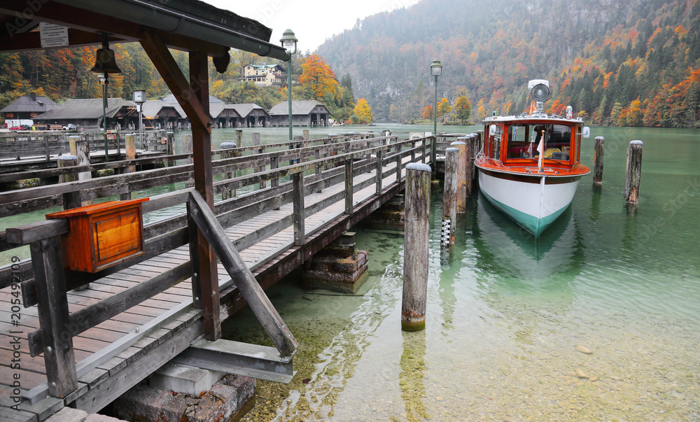 Obraz premium Sightseeing boat parking by a wooden pier at beautiful lakeside in a misty foggy morning on Lake Konigssee ~ Beautiful Autumn scenery of Koenigssee (King's lake) in Bavaria, Germany