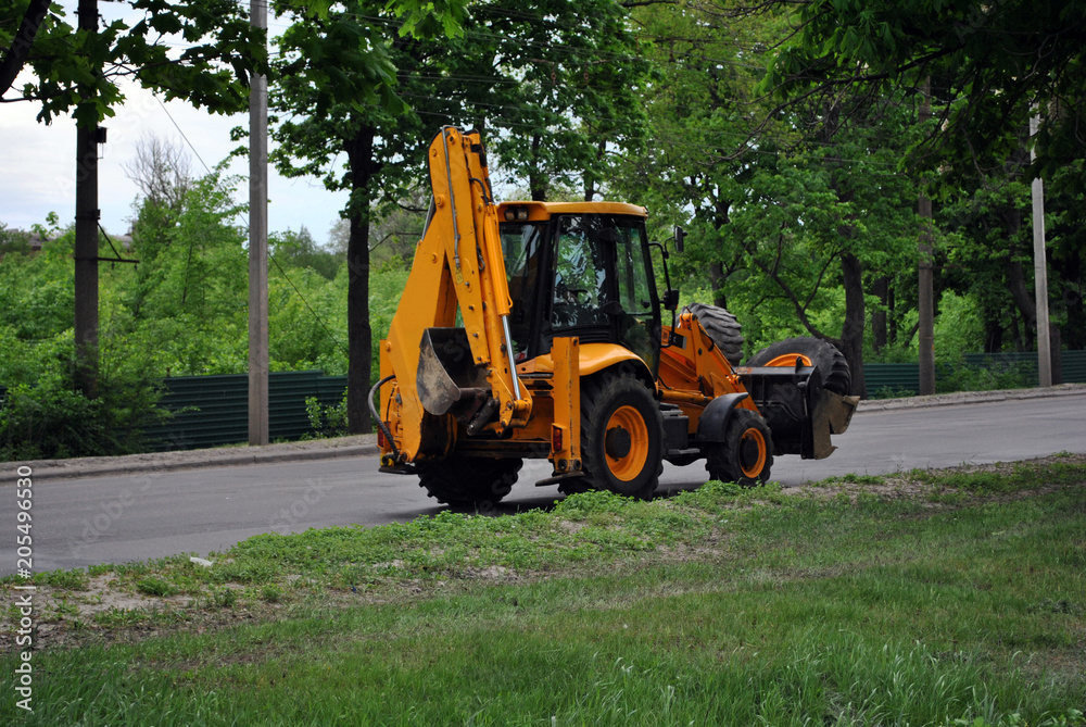 Bright orange excavator tractor on the road along park, spring in Kharkiv, Ukraine
