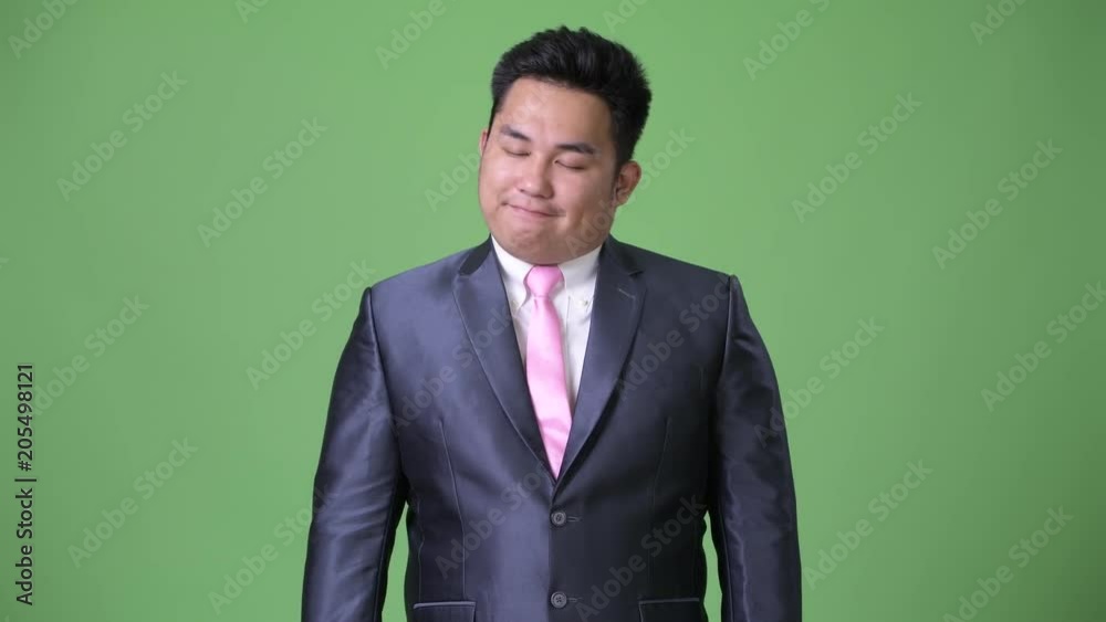 Young handsome overweight Asian businessman against green background Young handsome overweight Asian businessman against green background