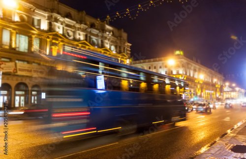 Movement of a blurred blue bus on the avenue at night.