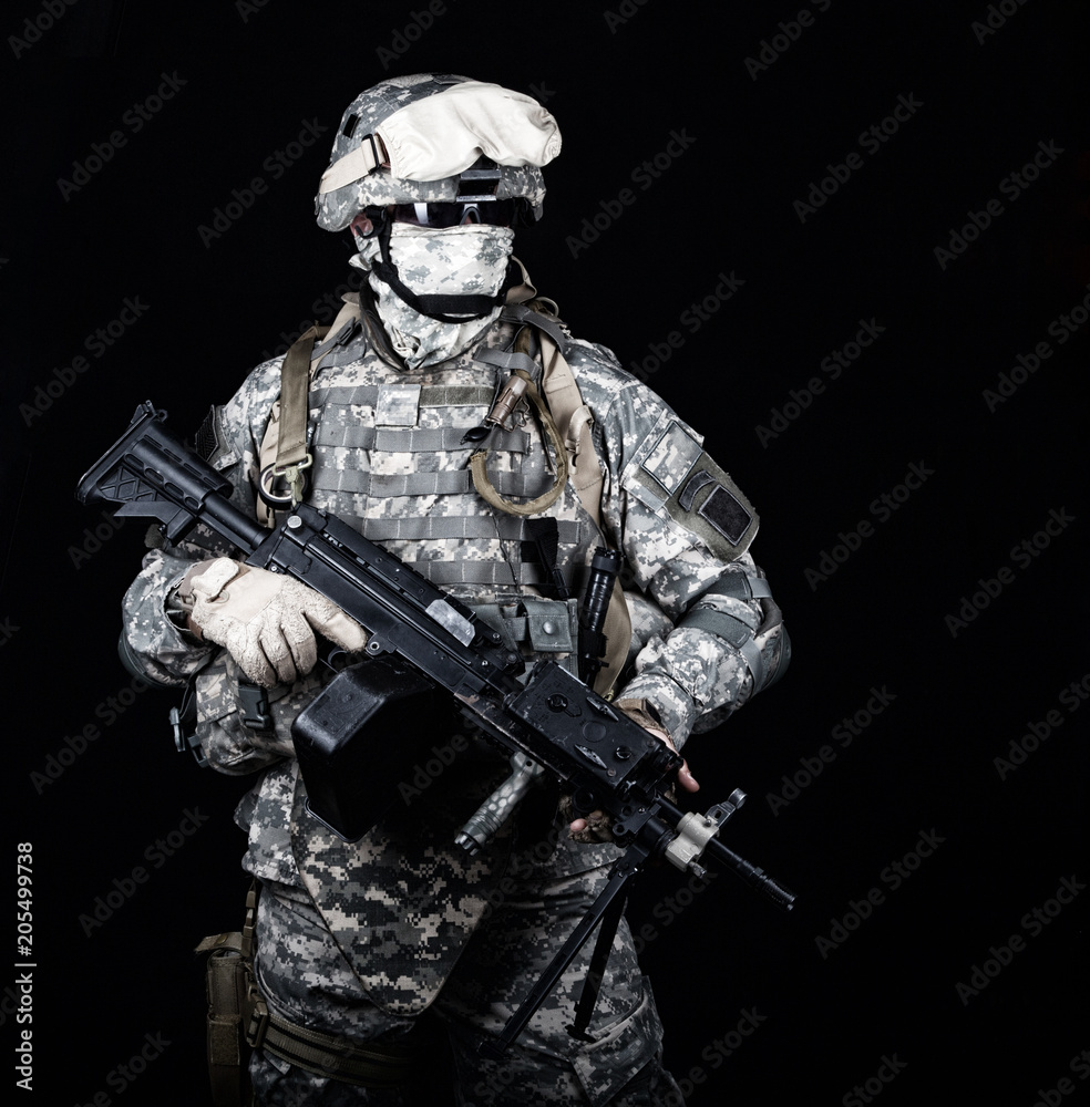 Marine with hiding identity, protected with helmet and body armour in digital camouflage combat uniform posing with light machine gun equipped infrared laser aiming light isolated on black background Marine with hiding identity, protected with helmet and body armour in digital camouflage combat uniform posing with light machine gun equipped infrared laser aiming light isolated on black background