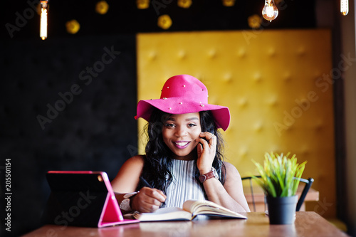 African american business woman in hat sitting at cafe and working.