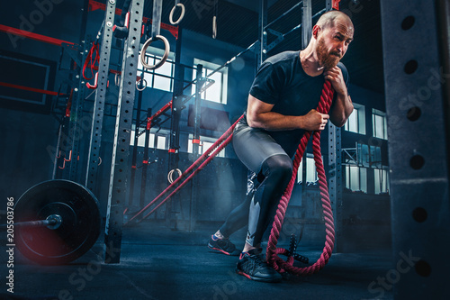Men with battle rope battle ropes exercise in the fitness gym. CrossFit.