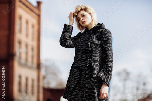 Fashion woman photo of young pretty girl touching her hair and posing outdoor in coat, spring street fashion photo