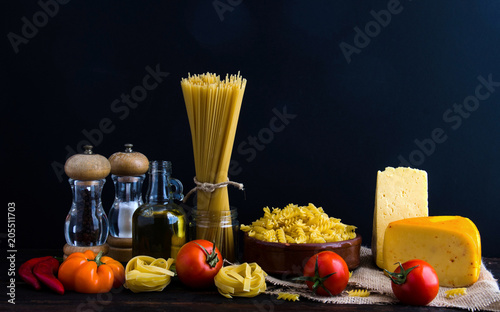 Different kinds of macaroni , oil , cheese , and tomatoes on a wooden table