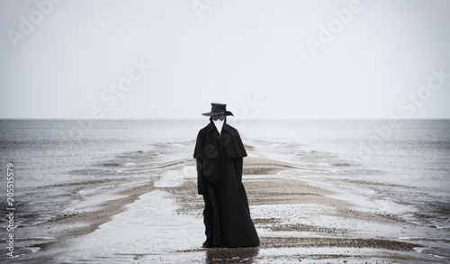 Plague doctor in seaside. Outdoor portrait with dramatic sky in background.