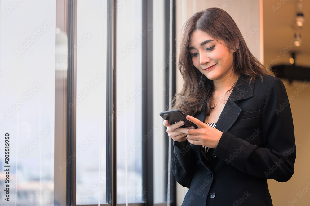 Asean office woman smiling during chat via smatphone nereby windows in the office.. Asean office woman smiling during chat via smatphone nereby windows in the office..