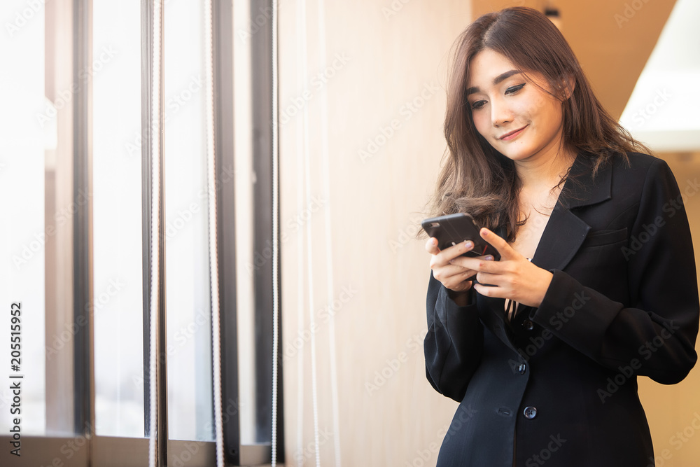 Asean office woman smiling during chat via smatphone nereby windows in the office.. Asean office woman smiling during chat via smatphone nereby windows in the office..