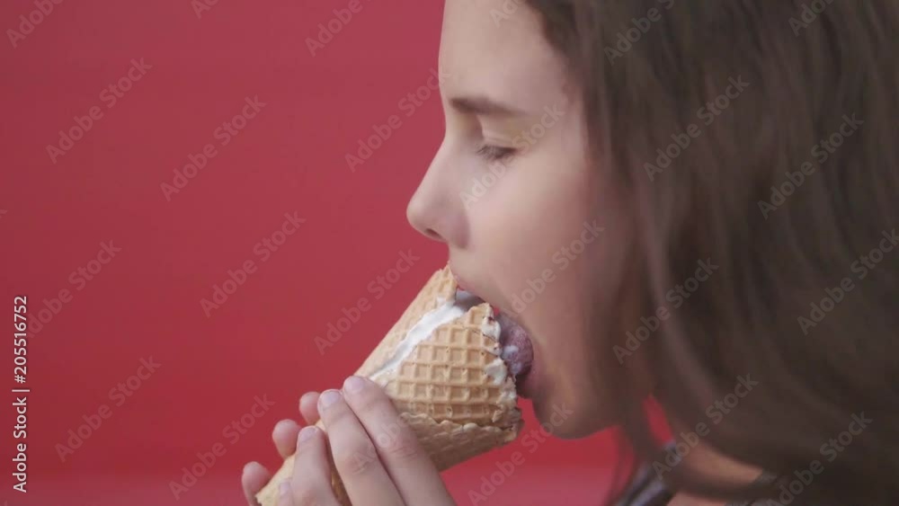 Pretty baby girl kid eating slow motion video nursing bottle licking big ice cream in waffle cone with lifestyle raspberry happy laughing on red background. the girl teenager and ice cream concept