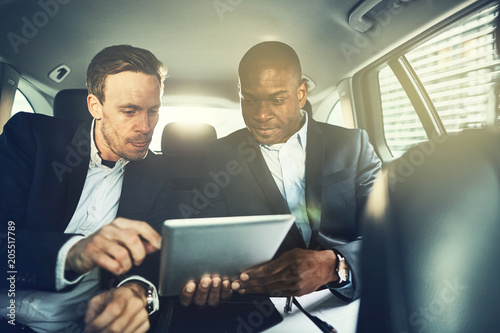 Businessmen sitting in the backseat of a car working online