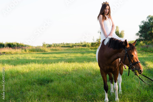 charming girl in white dress sitting on horse in the field 